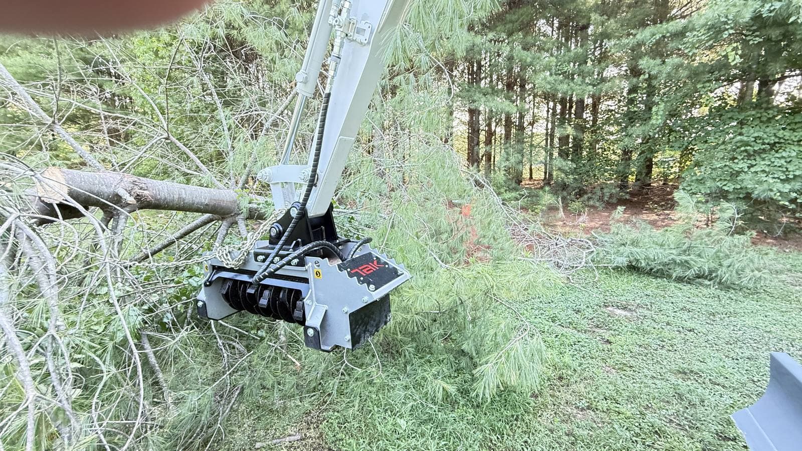 Close-up of a 31-inch fixed-tooth forestry mulching head on a mini excavator boom beside a cut pine limb